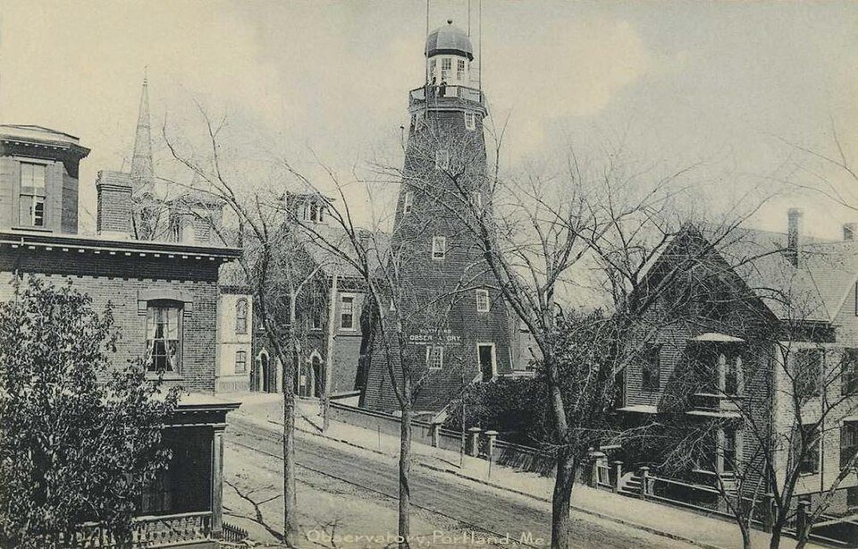 Una fotografía de postal antigua de la torre del observatorio sobre las casas y árboles sin hojas de una calle de Portland