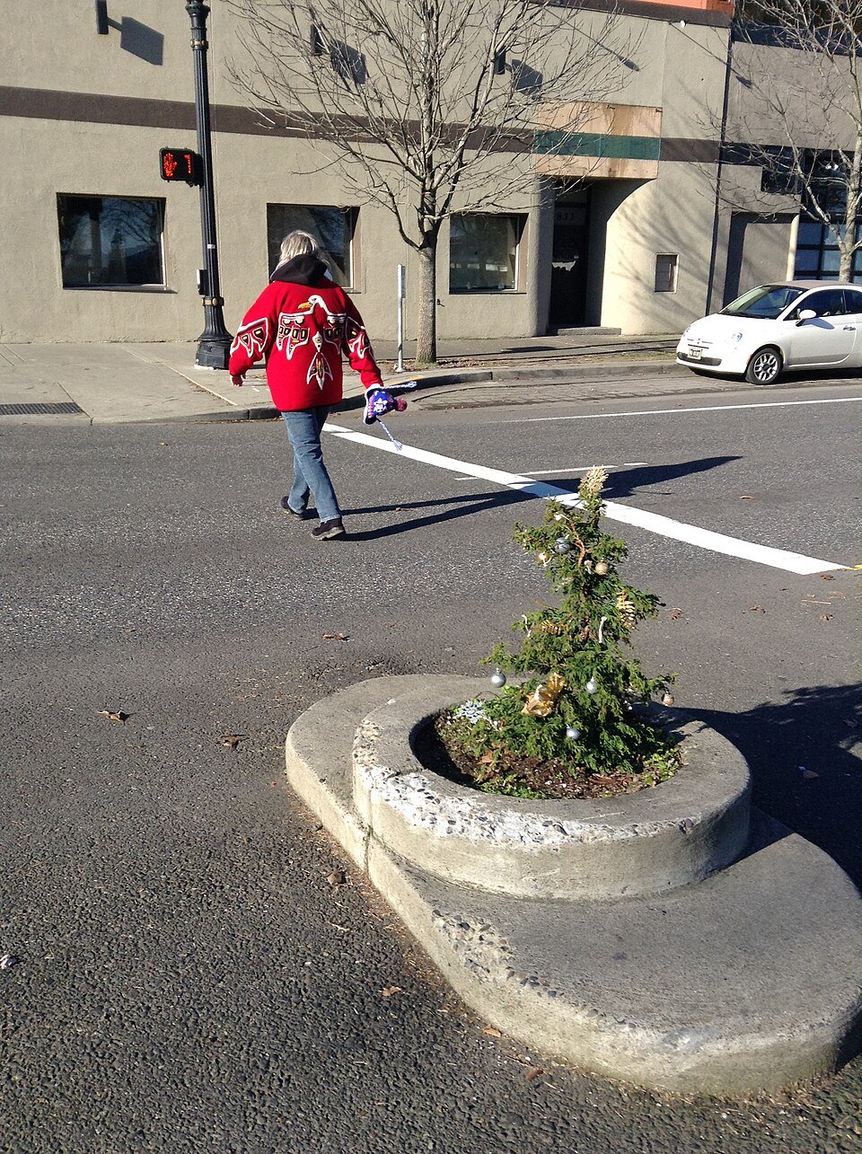 The park with a small tree hung with ornaments in December 2015, as a pedestrian crosses the street