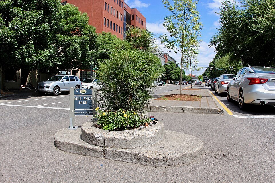 Mill Ends Park, a tiny round planter with flowers and a tall plant on a street median, with its blue park sign beside it