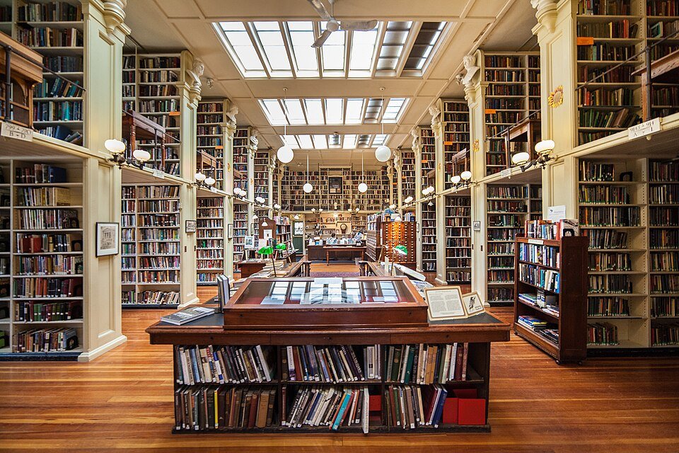 Sala de lectura con altas estanterías de madera, claraboyas y una vitrina de cristal