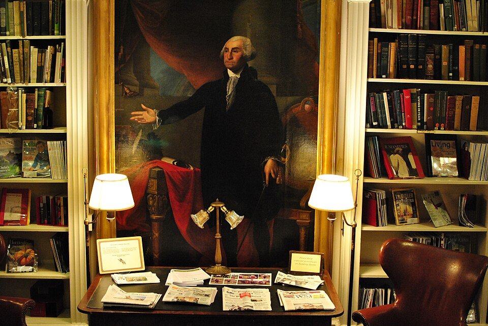 Gran retrato de George Washington colgado entre estanterías, sobre una mesa de lectura