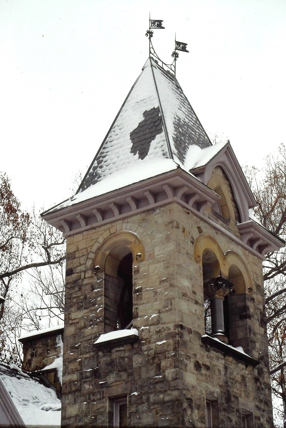 A torre de sinos de pedra da casa de entrada, coberta de neve, com campanário de arcos e telhado de ardósia