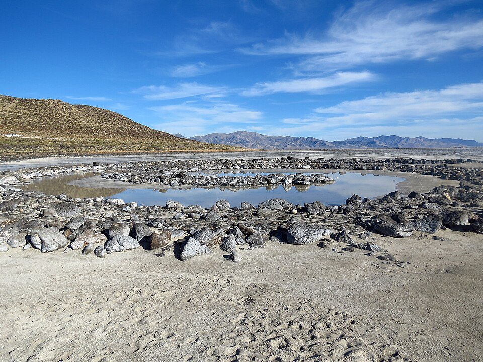 Rochas da Spiral Jetty em torno de uma poça de água, com montanhas ao fundo