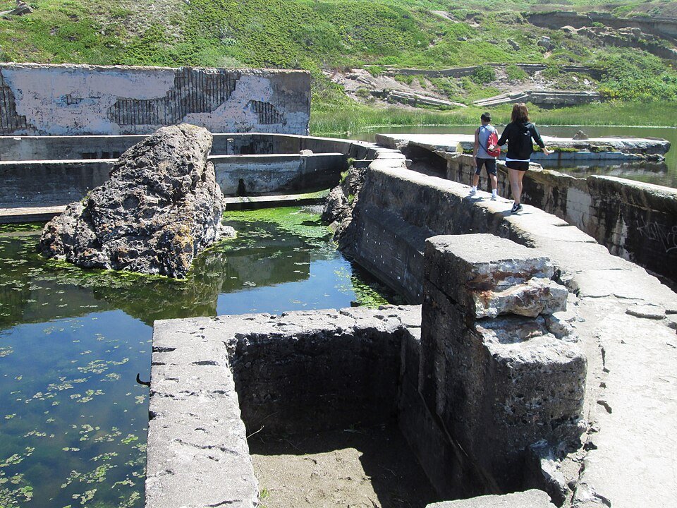 Visitantes caminando por un muro de hormigón entre piscinas en las ruinas de Sutro Baths en 2017
