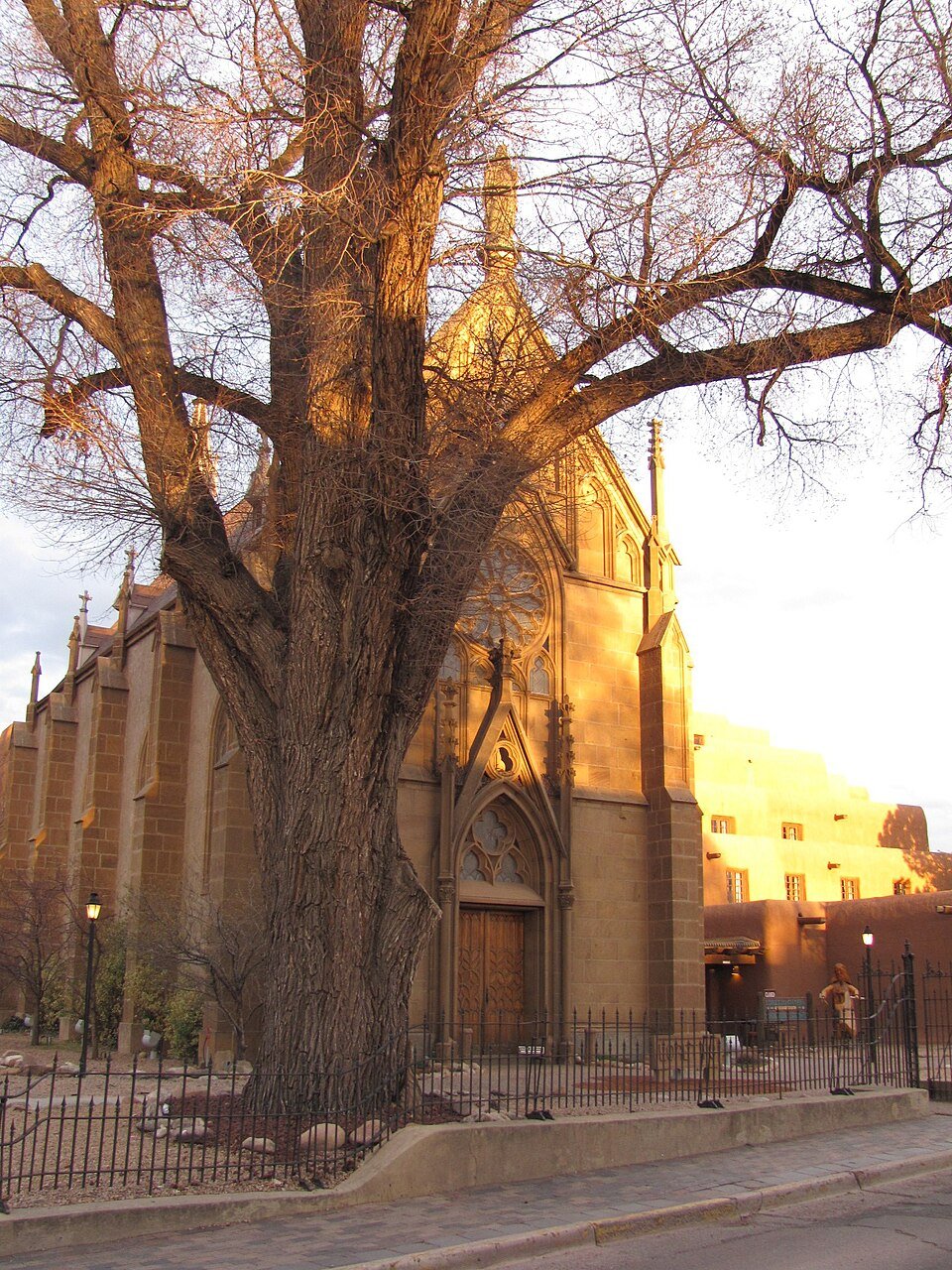 La fachada de Loretto Chapel al atardecer, detrás de un árbol grande y sin hojas