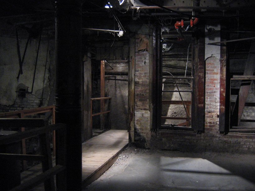 A dim, brick-walled basement room with a wooden walkway in the Seattle Underground