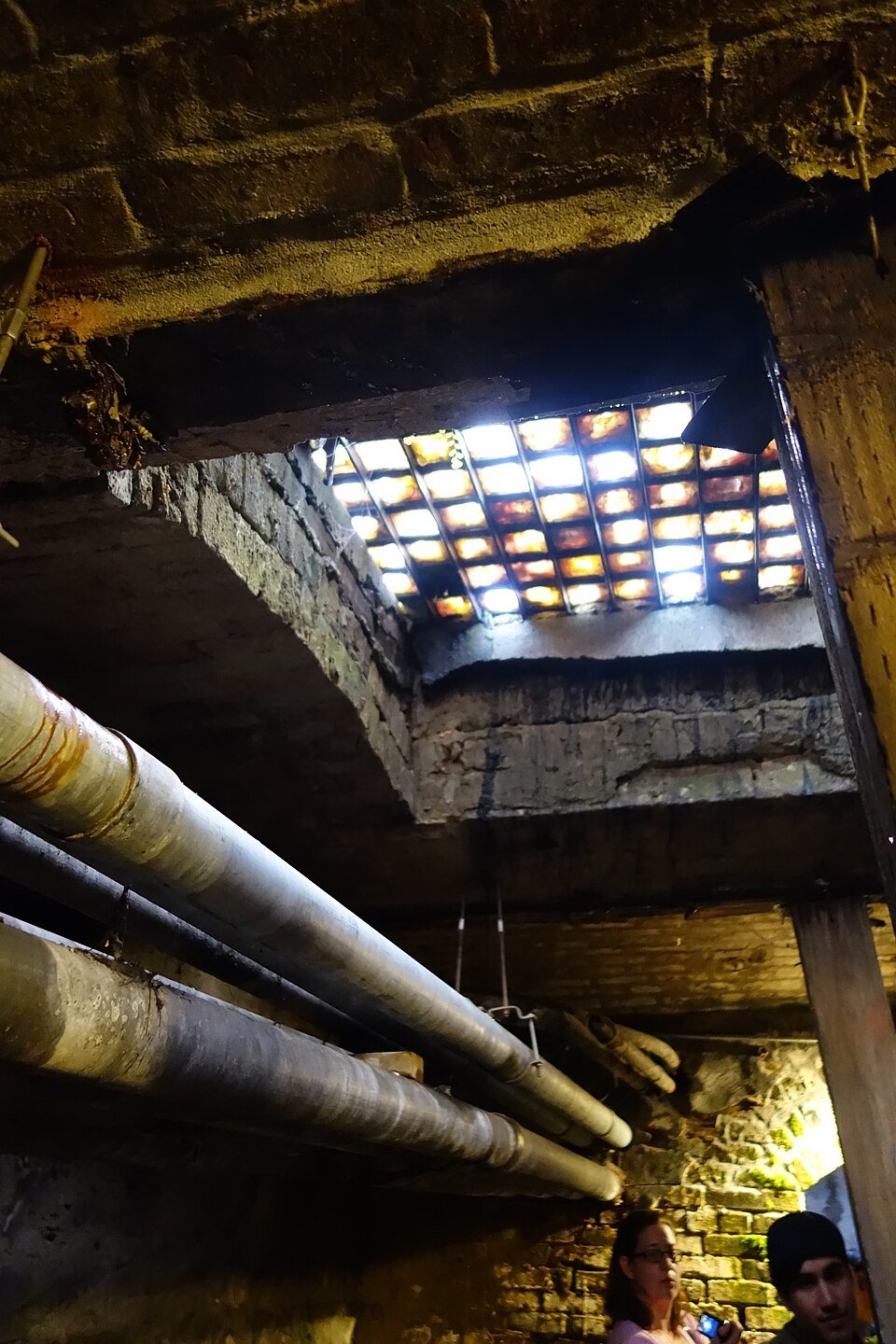 Vault lights seen from below in the Seattle Underground, above pipes and a brick arch