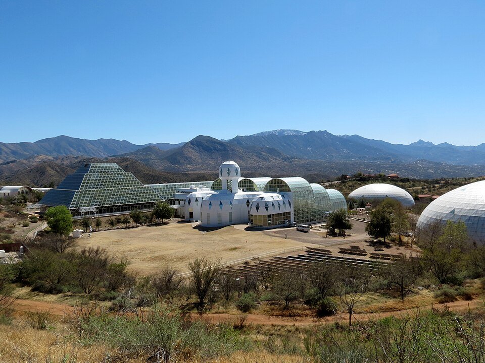 The Biosphere 2 campus seen from a hillside, with the glass pyramid, white domes and mountains behind