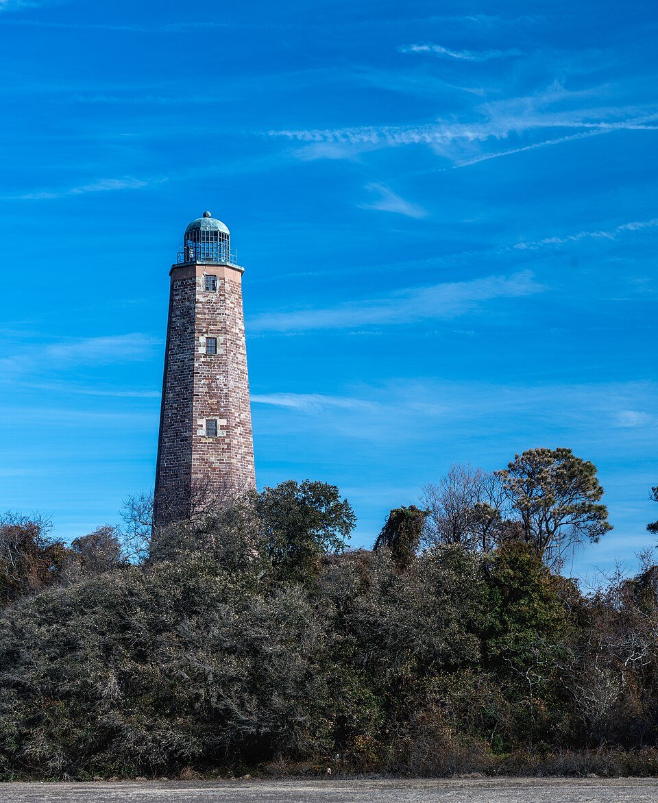The old Cape Henry Lighthouse rising above coastal shrubs under a blue sky