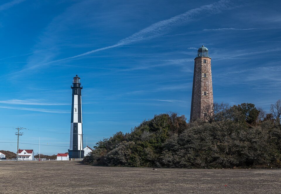 The new black-and-white lighthouse and the old sandstone tower side by side across an open field