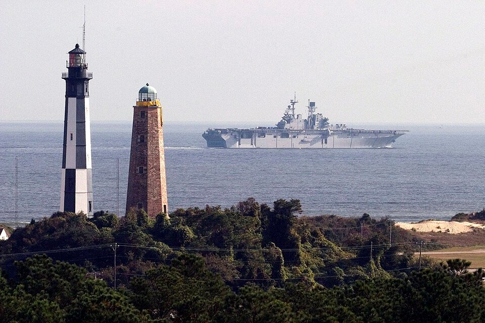 The two lighthouses on the Cape Henry shore with a large gray ship on the water behind
