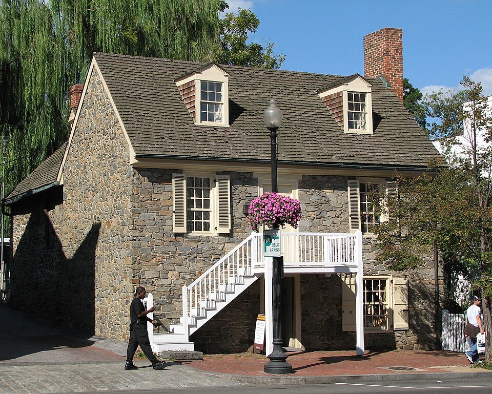 The Old Stone House in Georgetown, a two-story fieldstone house with dormer windows and a white outdoor staircase, beside a street