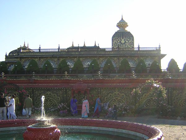 Vista lateral do Palace of Gold de Prabhupada, com uma fonte e visitantes em primeiro plano e uma cúpula com padrões dourados ao fundo
