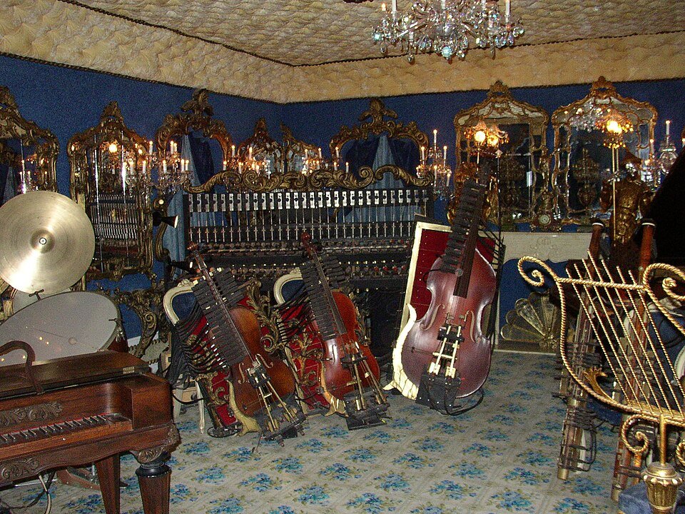Instrumentos musicais automáticos, entre eles violinos e um prato, em uma sala com espelhos dourados da House on the Rock